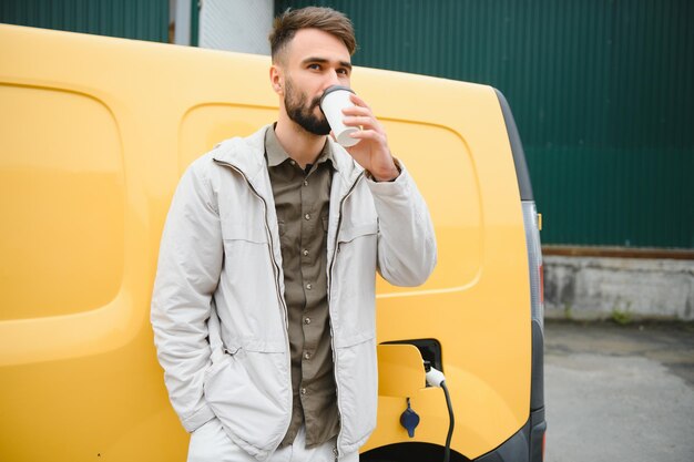 Фото Красивый мужчина пьет кофе во время зарядки электромобиля