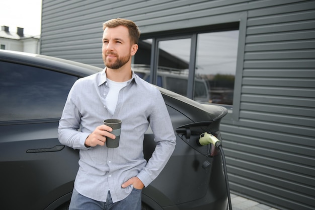 電気自動車を充電しながらコーヒーを飲んでいるハンサムな男性