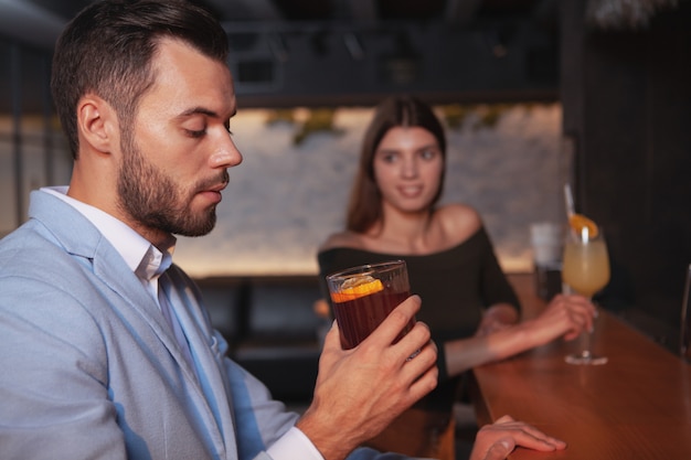 Uomo bello che beve cocktail di whisky, donna che lo guarda seducente