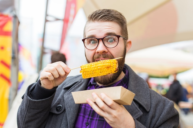 Фото Красивый мужчина ест вкусные кукурузные початки на улице.