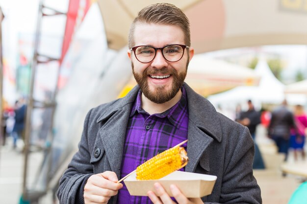 Uomo bello che mangia mais arrostito per strada.