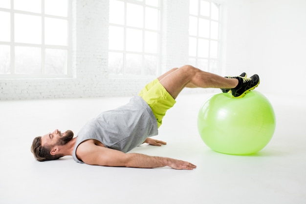 Handsome man exercising with fitball in the white gym interior