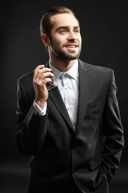 Handsome man in formal suit and with bottle of perfume on dark