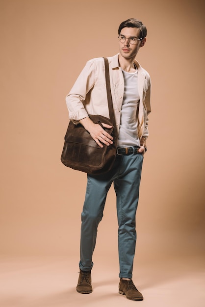 Handsome man in glasses standing with hand in pocket on beige background