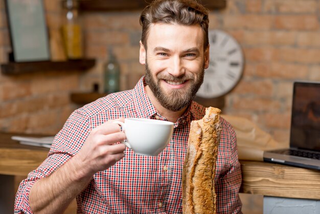 Handsome man having breakfast with coffee and baguette at the kitchen