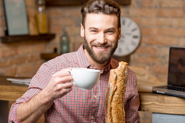 キッチンでコーヒーとバゲットと一緒に朝食をとっているハンサムな男