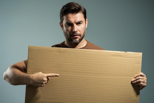 Photo handsome man holding empty board and pointing finger on board guy showing blank board with copyspace