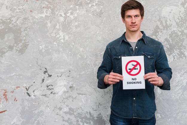 Photo handsome man holding no smoking banner standing near weathered wall