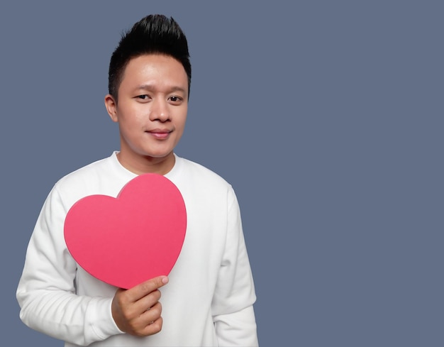 Handsome man holding and showing red heart shape with one hand