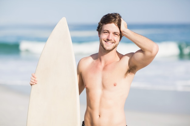 Handsome man holding surfboard on the beach