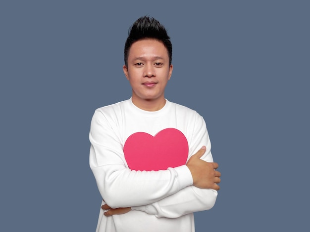 Handsome man hugging red heart shape isolated on plain background