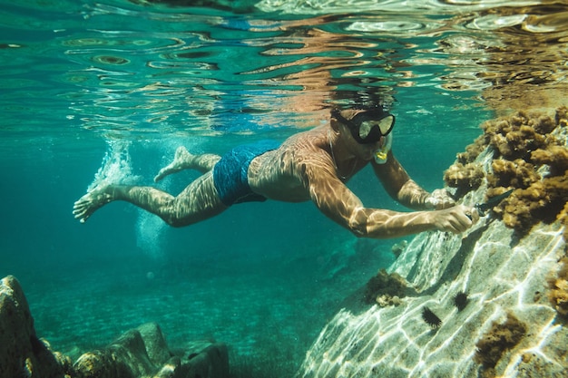 Un bell'uomo si diverte durante le vacanze estive ed esplora il fondale marino durante le immersioni subacquee in mare.