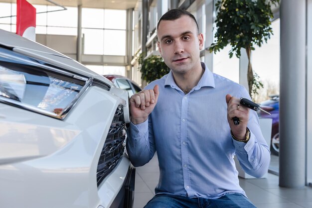 Handsome man is hugging his new car in showroom