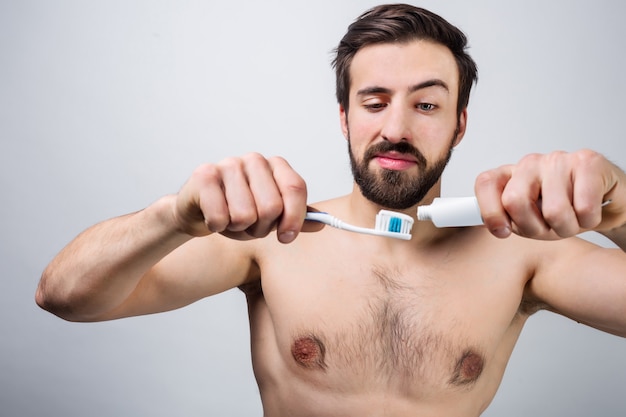 Foto bell'uomo si sta preparando a lavarsi i denti. sta mettendo del dentifricio sullo spazzolino da denti. avvicinamento. taglia vista.