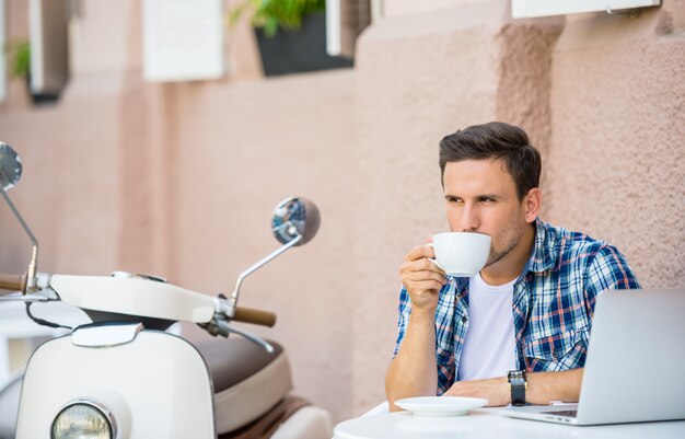 ハンサムな男はカフェでリラックスしてコーヒーを飲みます。