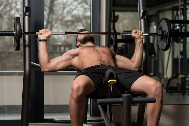 Handsome Man Is Working Out Chest With Barbell In A Modern Gym