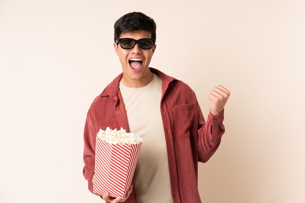 Handsome man over isolated background with 3d glasses and holding a big bucket of popcorns