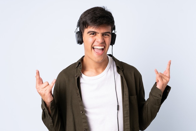 Handsome man over isolated blue listening music making rock gesture