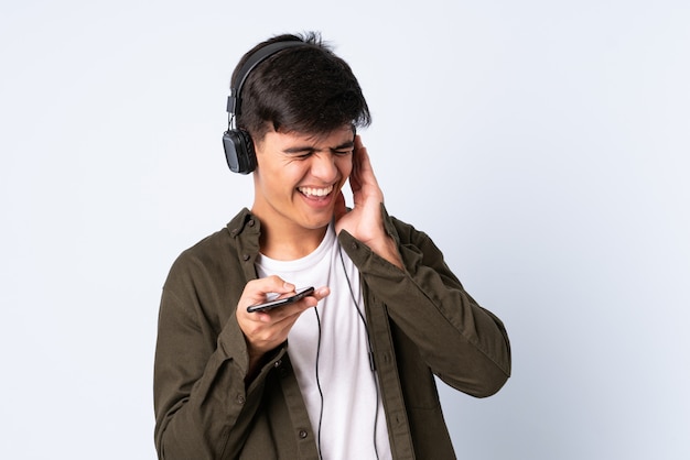 Handsome man over isolated blue listening music with a mobile and singing