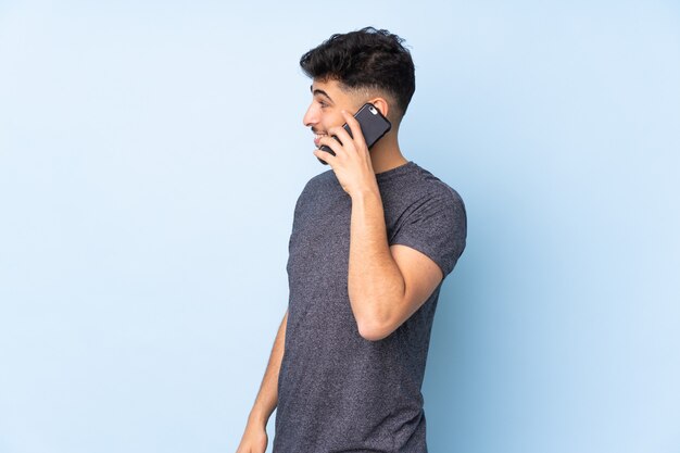 handsome man over isolated wall keeping a conversation with the mobile phone with someone