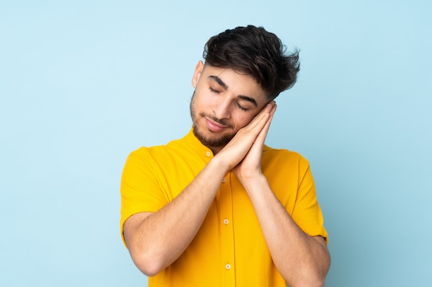 Uomo bello sopra la parete isolata che fa gesto di sonno nell'espressione dorable