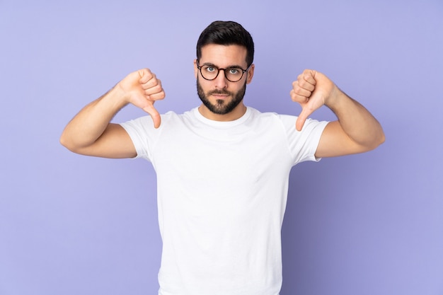 handsome man over isolated wall showing thumb down with two hands