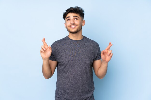 handsome man over isolated wall with fingers crossing and wishing the best