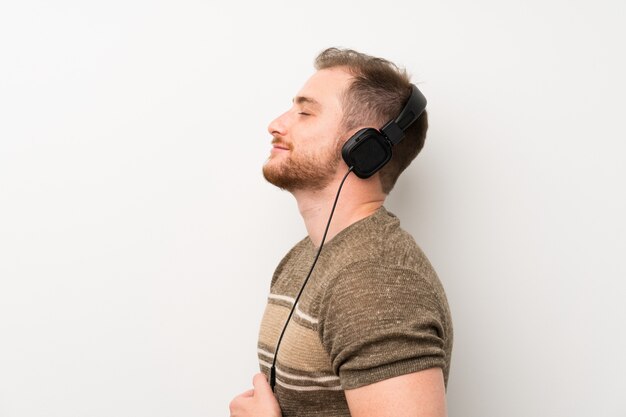 Handsome man over isolated white wall listening to music with headphones