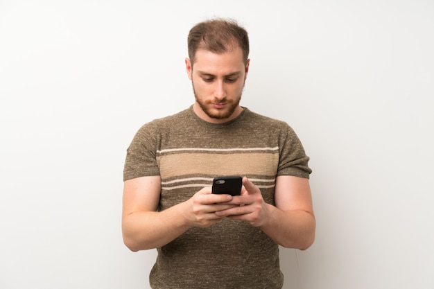 Handsome man over isolated white wall using mobile phone