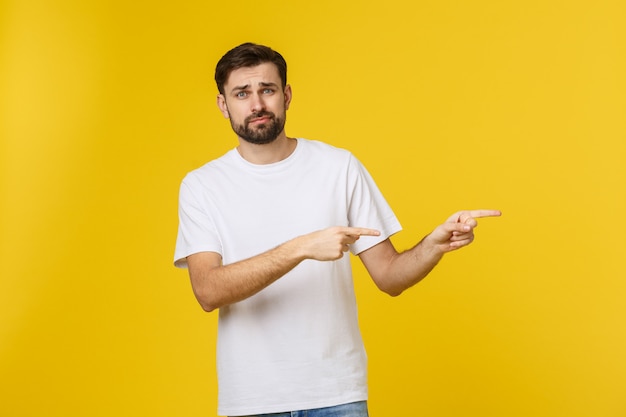 Uomo bello sopra la parete gialla isolata frustrata e che indica la parte anteriore.