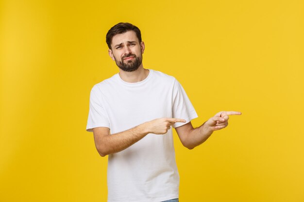 Uomo bello sopra la parete gialla isolata frustrata e che indica la parte anteriore.