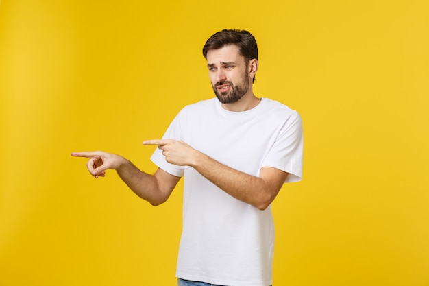 Uomo bello sopra la parete gialla isolata frustrata e che indica la parte anteriore.