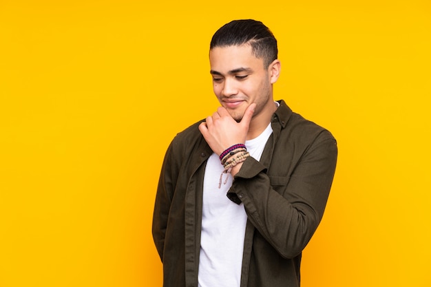 Handsome man isolated on yellow wall thinking an idea while looking up