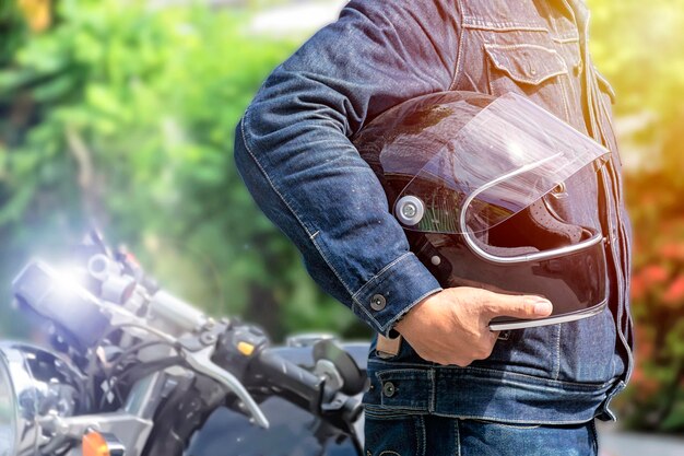 Photo handsome man in jean is standing near vintage motorcycle and holding a helmet to prepare to go to the destination