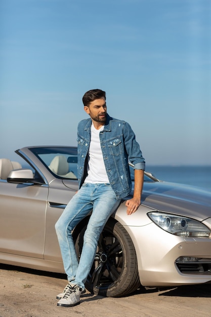 Handsome man leaning convertible and looking away