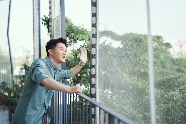 Handsome man leaning on rail waving from balcony