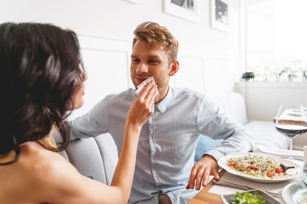 Фото Красивый мужчина смотрит на подруг и улыбается, пока она вынимает соус из уголка его рта
