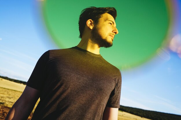 Handsome man looking away while standing on field against sky