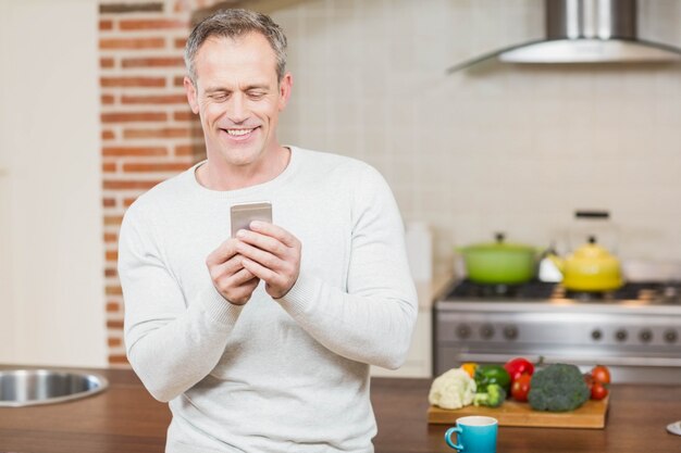 ハンサムな男が台所でスマートフォンを見て