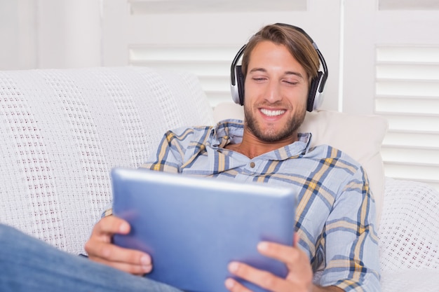 Handsome man lying on couch listening to music on tablet pc