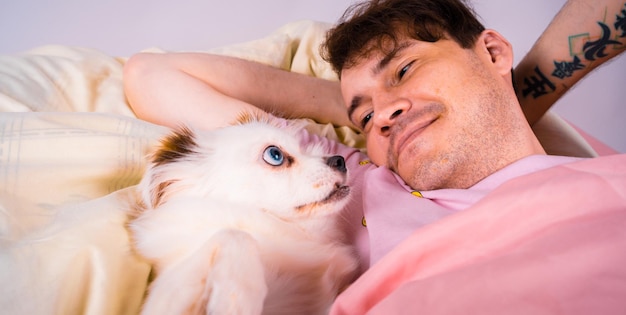 Handsome man lying with little white dog with blue eyes at bed\
young man in a bed under a rug with his dog in an embrace handsome\
young hipster with his dog resting on bed at home