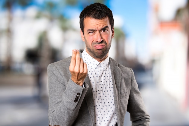 Handsome man making money gesture on unfocused background