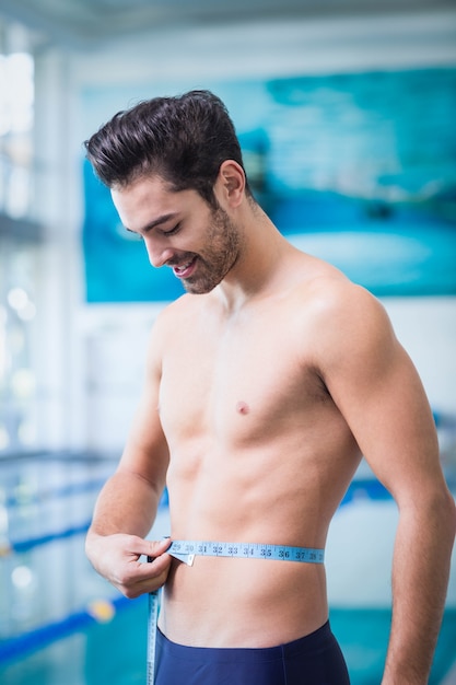 Handsome man measuring waist in the swimming pool