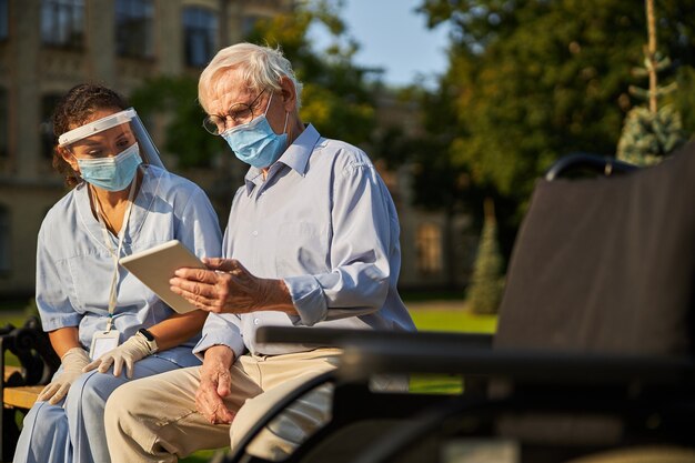 Handsome man in medicine mask spending time with adult woman in the outdoors