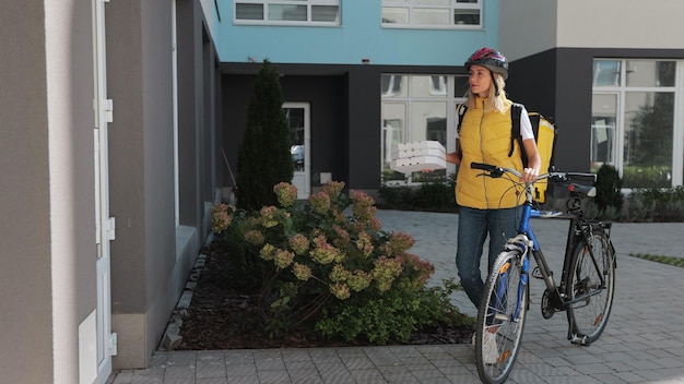 Handsome man open door to a pizza delivery woman wearing yellow thermal backpack on a bike and recieves cardboard boxes of pizza Food delivery concept