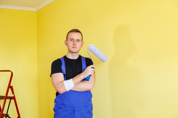 Handsome man in overalls hold paint roller,. tools accessories\
for apartment room renovation. home renovation concept