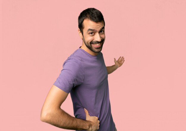 Handsome man pointing back and presenting a product on isolated pink background