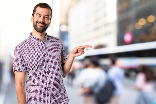 Handsome man pointing to the lateral on unfocused background