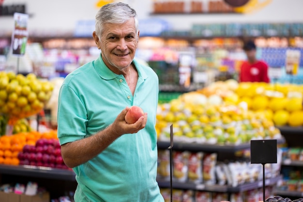 Handsome man posing, looking and holding fruit in hand. Bearded customer smiling. Section with fresh citruses on space.