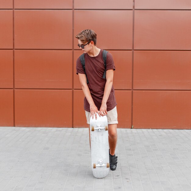 Handsome man posing with skateboard near the wall